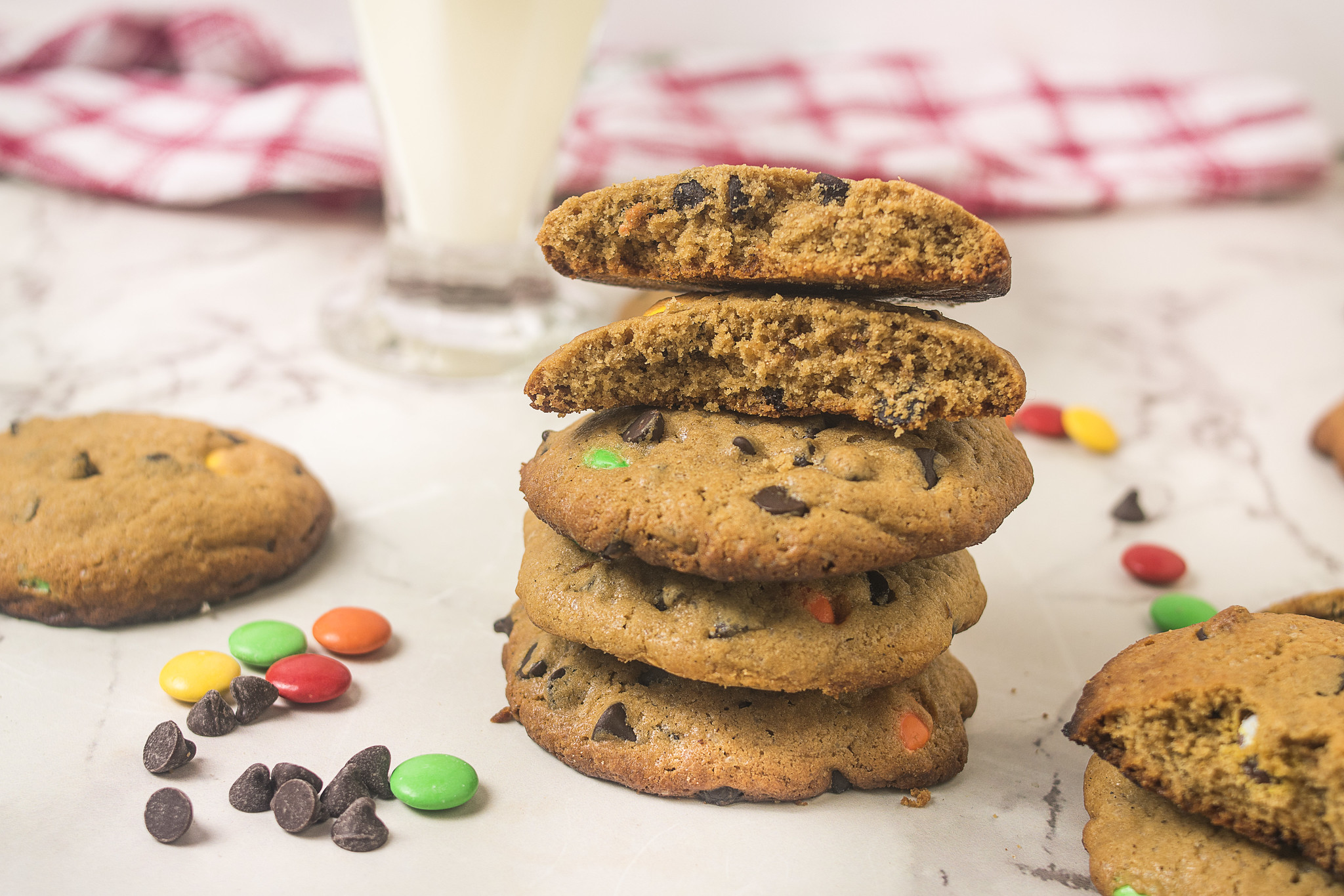 Stack of browned butter chocolate chip cookies with chocolate chips and M&Ms, topped with two cookies broken open to show the centres.